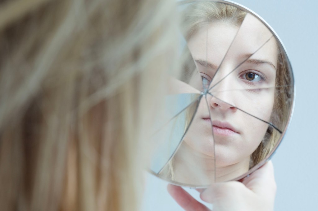 A woman looking at a broken mirror